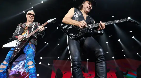 Dwóch gitarzystów na scenie, jeden w skórzanej kurtce i niebieskich spodniach, drugi w czarnej kamizelce i skórzanych spodniach. Ich gra wywołuje "wind of change" tłumaczenie.