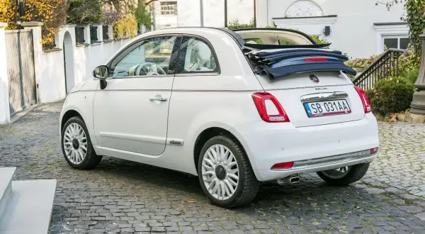 Biały fiat 500c cabrio z otwartym dachem stoi na brukowanej uliczce.