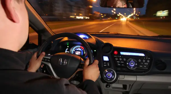 Kierowca prowadzi auto nocą. Czy w czasie jazdy w nocy masz obowiązek zwiększyć uwagę? Widok z wnętrza pojazdu na drogę i deski rozdzielcze.
