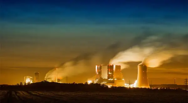 Dymiące kominy elektrowni nocą, ukazujące przyczyny zanieczyszczenia powietrza.