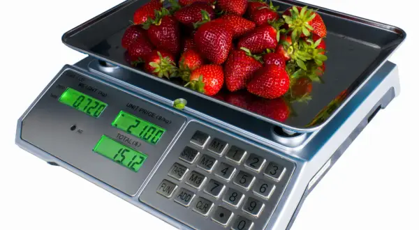 Kobiałka pełna soczystych truskawek waży się na wadze cyfrowej, pokazując 0.720 kg.