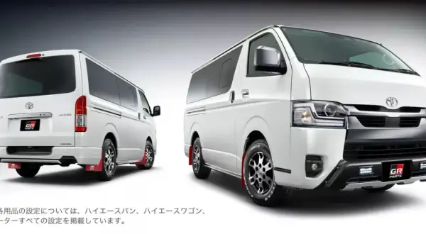 Dwa białe vany Toyota Hiace z pakietem GR Parts. Jeden z tyłu, drugi z przodu, oba z czerwonymi chlapacami.