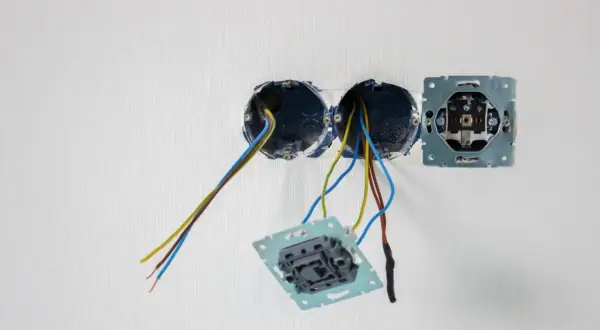 Osadzanie puszek elektrycznych w ścianie. Widać przewody wychodzące z dwóch puszek, a obok zamontowaną ramkę gniazdka.