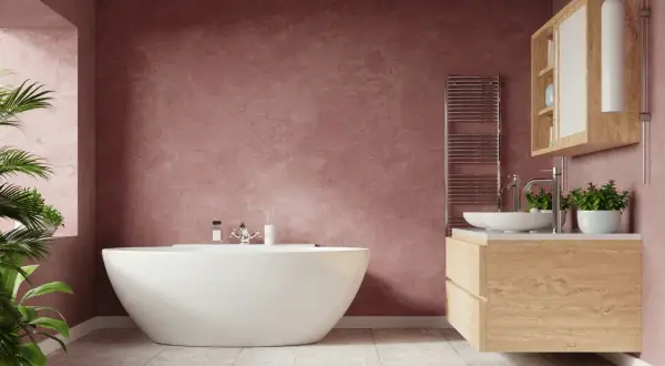 Un baño moderno con bañera independiente y tocador de madera. Las paredes de color rosa empolvado y las plantas aportan un toque acogedor a estos baños rústicos.