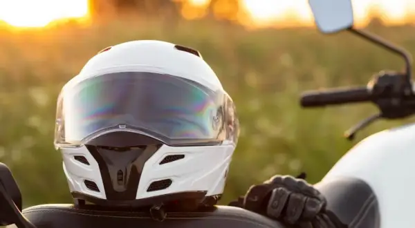 Biały kask motocyklowy i rękawice na siedzeniu motocykla podczas zachodu słońca.