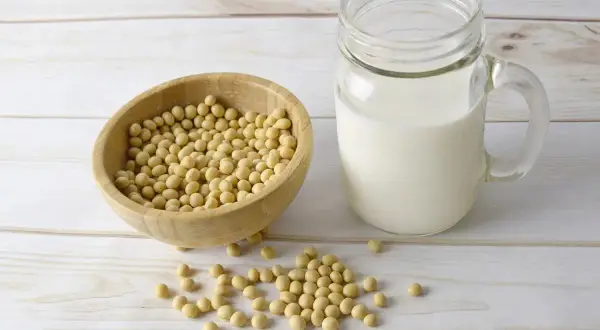 Bol en bois rempli de graines de soja à côté d'un verre de lait de soja. Découvrez les lécithine de soja bienfaits pour votre santé.