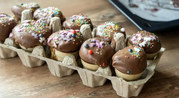 Schokoladenüberzogene Waffelbecher Kuchen mit bunten Streuseln und Zuckerfiguren in einer Eierpappe.