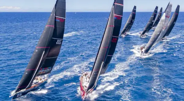 Diverse barche a vela nere con vele rosse e bianche competono in una regata, solcando le onde blu con determinazione.