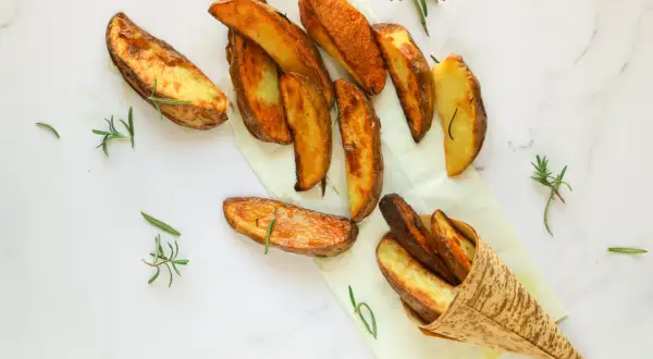 Patate al forno dorate e croccanti, profumate al rosmarino, servite su carta da forno e in un cono di bambù.