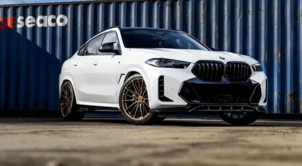 Białe BMW X6 z brązowymi felgami, na których zamontowano opony Imperial, prezentuje się imponująco na tle niebieskiego kontenera.