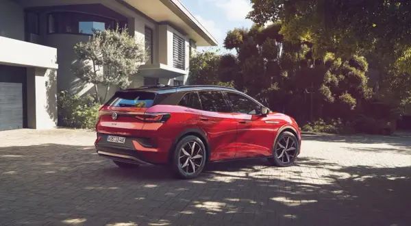 Röd elbil parkerad på uppfart framför modernt hus. En dag för att fundera på hur många elbilar som finns i Sverige.