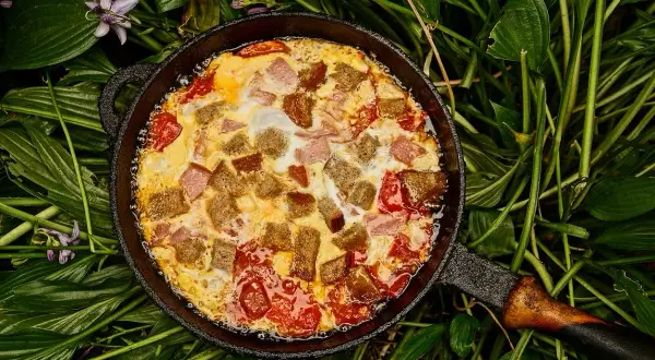 Pyszna kolacja z jajek z pomidorami i grzankami w żeliwnej patelni, otoczona zielonymi liśćmi.