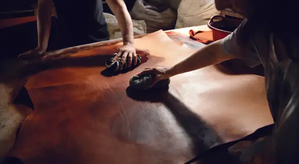 Mani esperte lavorano il cuoio con cura, un processo di lavorazione cuoio artigianale che dona profondità e colore alla pelle.