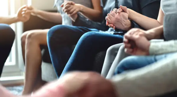 Un círculo de mujeres y hombres tomados de la mano, compartiendo un momento de conexión y apoyo mutuo.