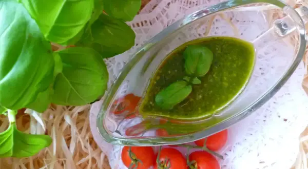 Aromatyczne pesto bazyliowe w sosjerce, ozdobione listkami bazylii, obok gałązki pomidorków koktajlowych.