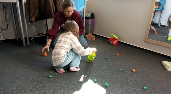 Terapeuta pomaga dziecku w zabawie, która jest częścią wczesnego wspomagania rozwoju.