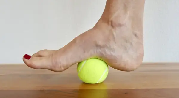Fuß auf einem Tennisball zur achillessehne dehnen. Sanfter Druck auf die Ferse zur Lockerung.