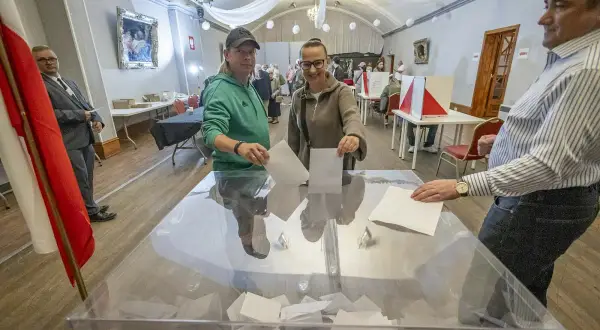 Ludzie oddają głosy w lokalu wyborczym, korzystając z czynnego prawa wyborczego. W tle widać flagę Polski.
