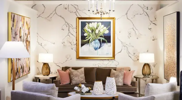 A living room with traditional interior design, featuring a floral wallpaper, a painting of tulips, a brown sofa, and plush armchairs.