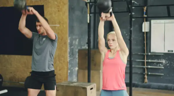 Uomo e donna eseguono esercizi con kettlebell, un allenamento completo per diversi gruppi muscolari in palestra.