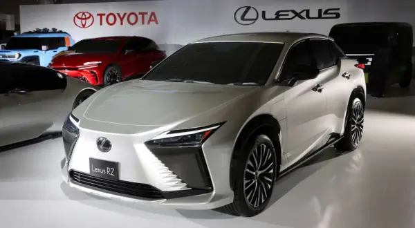 Elegancki, srebrny Lexus RZ prezentuje się na tle logo Toyoty i Lexusa.
