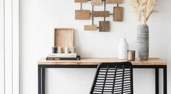 Un bureau en bois avec une chaise noire, des livres, des vases et une décoration murale. Idéal pour apprendre comment décalquer sur du bois.