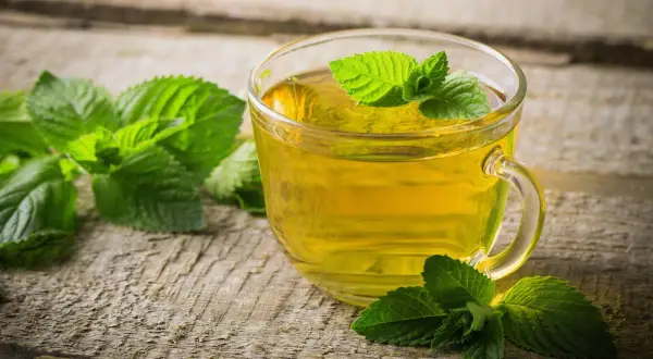 Une tasse de thé à la menthe, aux vertus et méfaits discutés, sur fond de bois vieilli.
