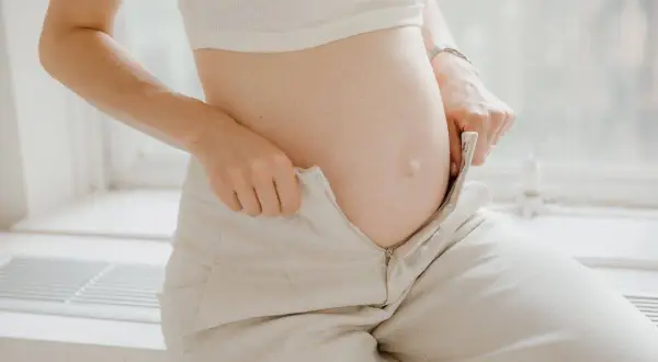 Barriga de embarazada, ajustando pantalones. Los cambios del embarazo, como los pedos, son parte de la experiencia.
