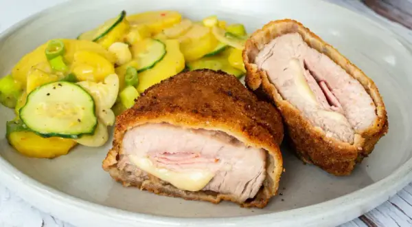 Zwei goldbraune Cordon-bleu-Schnitzel mit geschmolzenem Käse und Schinken, serviert mit einem Kartoffel-Zucchini-Salat.