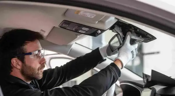 Un technicien porte des lunettes de sécurité et des gants pour démonter le rétroviseur intérieur. C'est le moment pour changer un pare-brise.