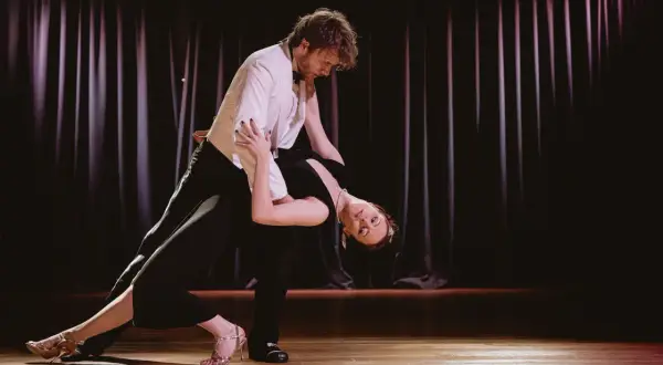 Para tańczy tango na scenie, kobieta w czarnej sukni w głębokim ukłonie, mężczyzna w białej marynarce.