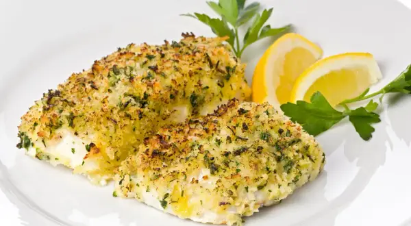 Delizioso merluzzo al forno con crosta dorata di pangrattato ed erbe aromatiche, guarnito con spicchi di limone e prezzemolo fresco.