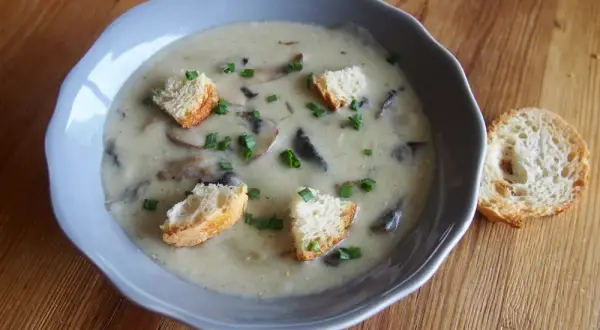 Un réconfortant velouté de champignon, garni de croûtons dorés et de ciboulette fraîche, servi dans un bol bleu sur une table en bois.