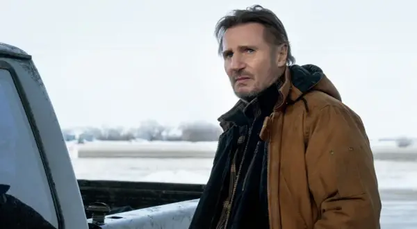 Liam Neeson w brązowej kurtce, w zimowej scenerii, jak w jego filmach.