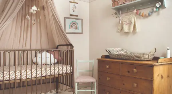 A serene modern nursery theme with a gold crib, cloud mobile, and rainbow art. A vintage dresser holds a woven basket, completing the cozy, dreamy atmosphere.