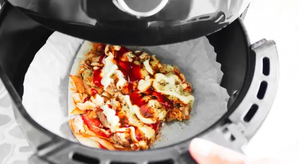 Odgrzewanie pizzy w piekarniku beztłuszczowym. Kawałek pizzy z kurczakiem, serem i sosami w koszu frytkownicy.