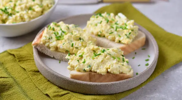 Pyszna pasta jajeczna jak dawniej, podana na kromkach chleba, posypana szczypiorkiem. Smak dzieciństwa na talerzu.