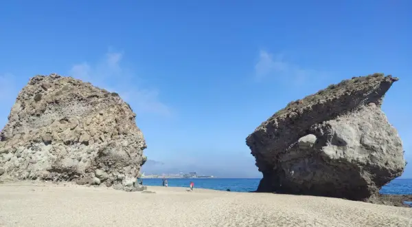 Dos rocas gigantes flanquean una playa de guijarros en la carbonera de Almería, con el mar azul y el cielo despejado de fondo.