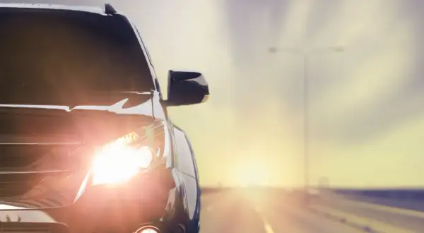 Las luces del coche brillan intensamente al amanecer en una carretera desierta.