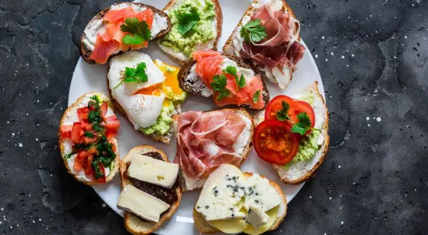 Talerz pełen pysznych sznytek: z łososiem, awokado, jajkiem w koszulce, szynką parmeńską, pomidorami i serami.