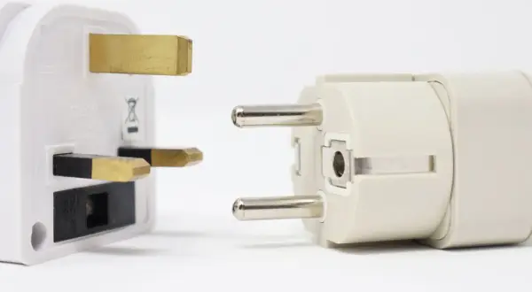 Adapter do gniazdek w Hiszpanii. Biały adapter z bolcami brytyjskimi obok jasnoszarego z bolcami europejskimi.
