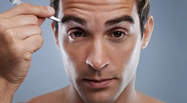 Uomo si sistema le sopracciglia con una pinzetta, cura del viso maschile.
