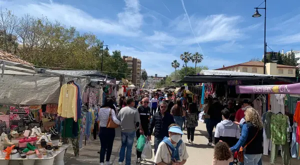 Folkmyller på marknad i Fuengirola. Stånd med kläder och skor längs en solig gata.