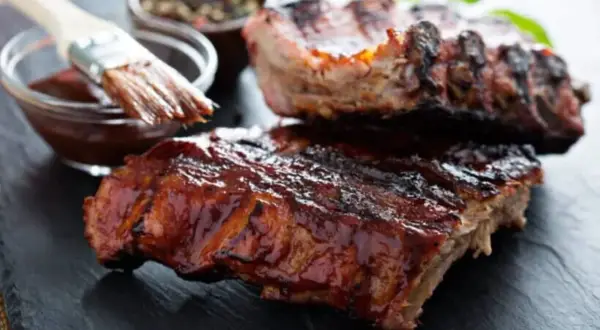 Saftige Rippchen, glasiert mit BBQ-Sauce. Ein Pinsel taucht in die Sauce, bereit für die Zubereitung: low and slow.