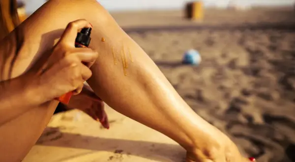 Kobieta aplikuje na nogę ulubiony samoopalacz gwiazd, by uzyskać idealną opaleniznę na plaży.