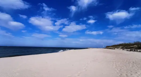 Pusta piaszczysta plaża nad Bałtykiem, błękitne niebo z chmurami, morze i wydmy.