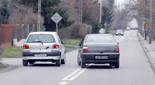 Srebrny samochód wyprzedza ciemny, jadący po tej samej drodze. Wymijanie i omijanie to kluczowe manewry na drodze.