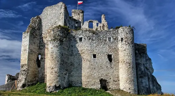 Ruiny zamku w Mirowie na tle błękitnego, chmurnego nieba. Biało-czerwona flaga powiewa na szczycie.