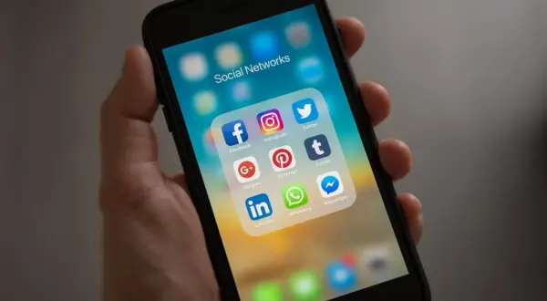 Dłoń trzyma smartfon z ikonami aplikacji społecznościowych. Widoczna ikona Facebooka, która pomoże Ci dowiedzieć się, jak dołączyć do grupy na FB.