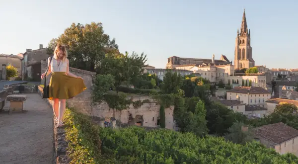 Donna passeggia su un muro a Saint-Émilion, con il villaggio e la sua chiesa in lontananza.